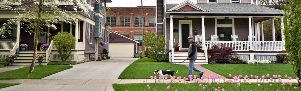 man walking dog on street in front of nice porch on home