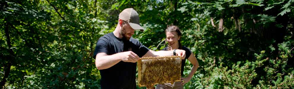 man and woman standing together holding a beehive frame