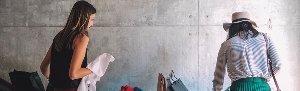 two girls shopping together holding up clothes