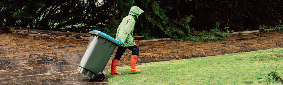 person in rain coat and rain boots taking out the garbage