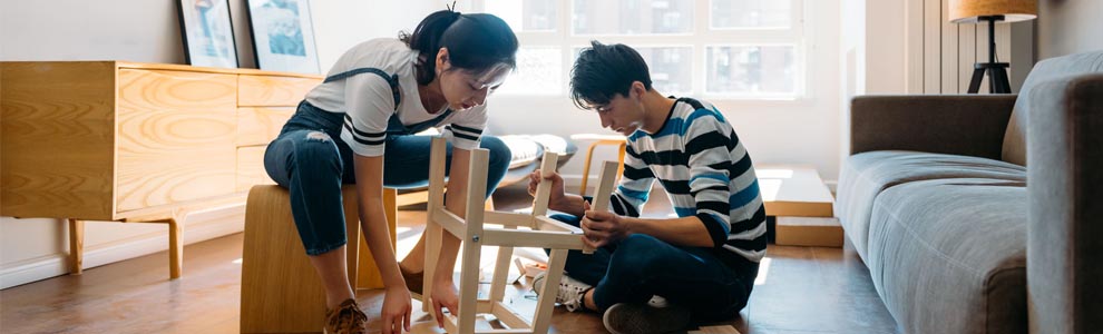 two young adults sitting on floor of empty apartment building stool