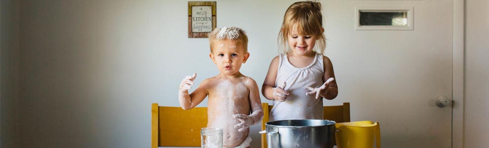 two children making a mess in the kitchen with flour