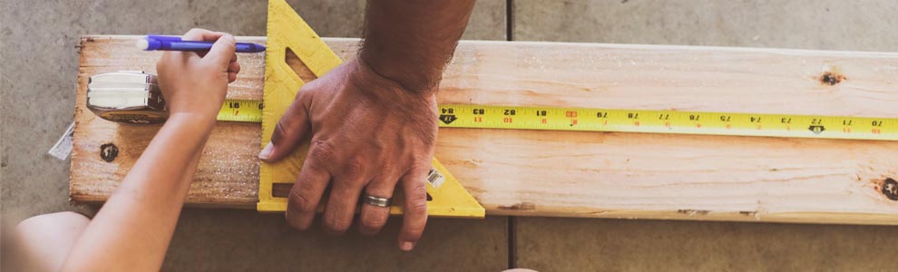 two people measuring and marking a piece of wood